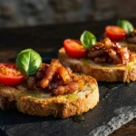 Crostini com guanciale B12 finalizados sobre ardósia com tomate cereja, manjericão e fio de azeite