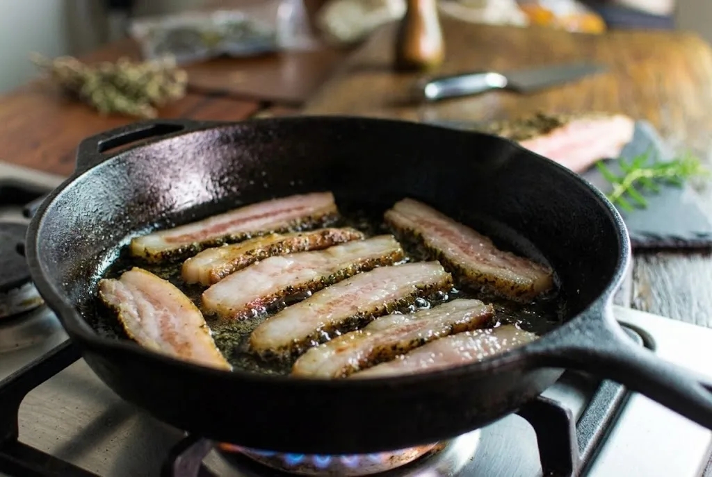 Guanciale B12 em tiras sendo frito em frigideira para o carbonara — gordura derretendo em fogo baixo
